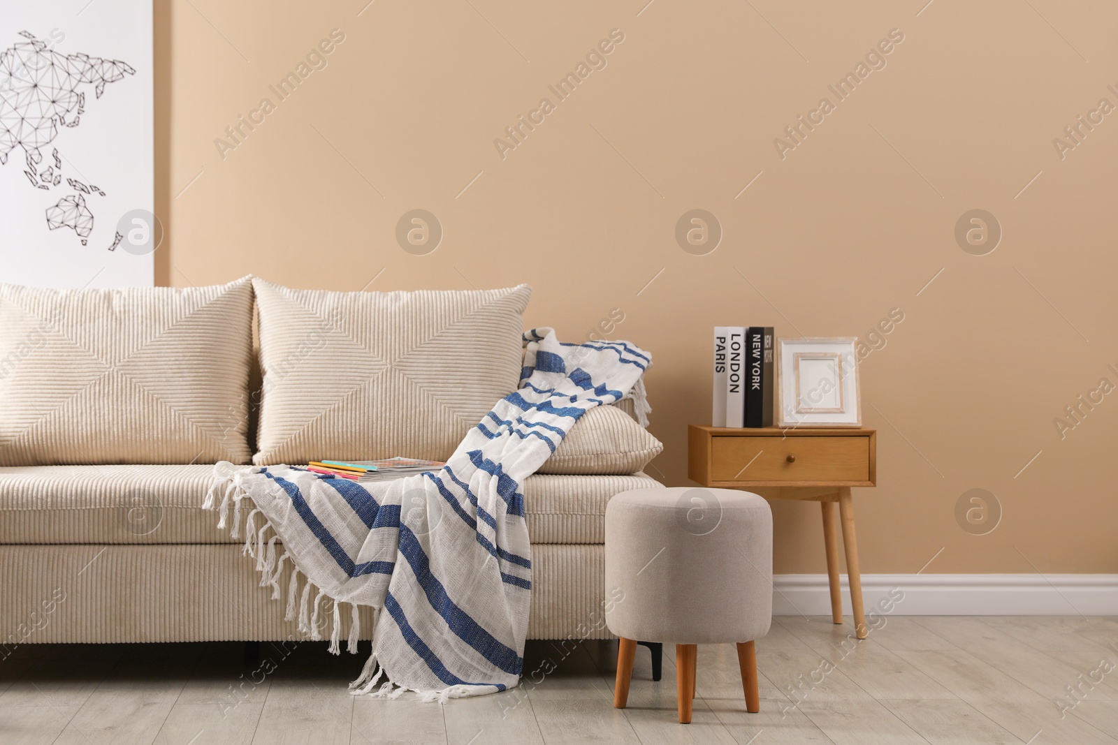 Photo of Comfortable sofa with pillows, blanket, pouf and bedside table near beige wall indoors