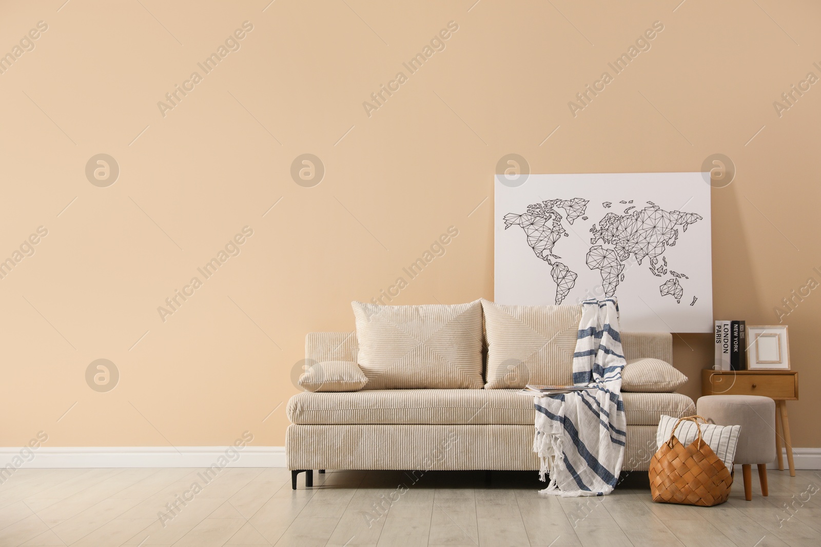 Photo of Comfortable sofa with pillows, blanket, pouf and picture indoors, space for text