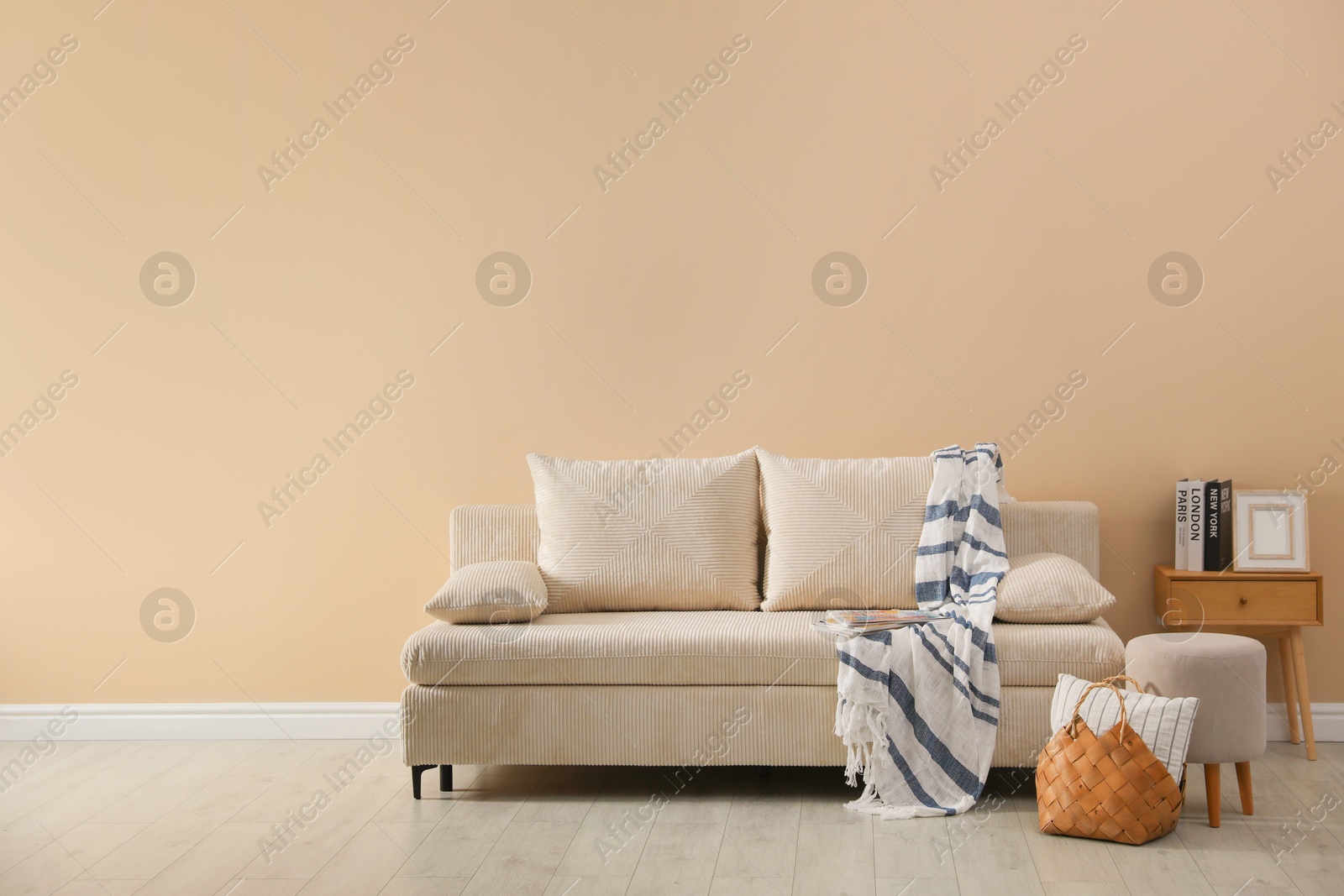 Photo of Comfortable sofa with pillows, blanket, pouf and bag indoors, space for text