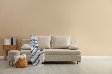 Photo of Comfortable sofa with pillows, blanket, pouf and bag indoors, space for text