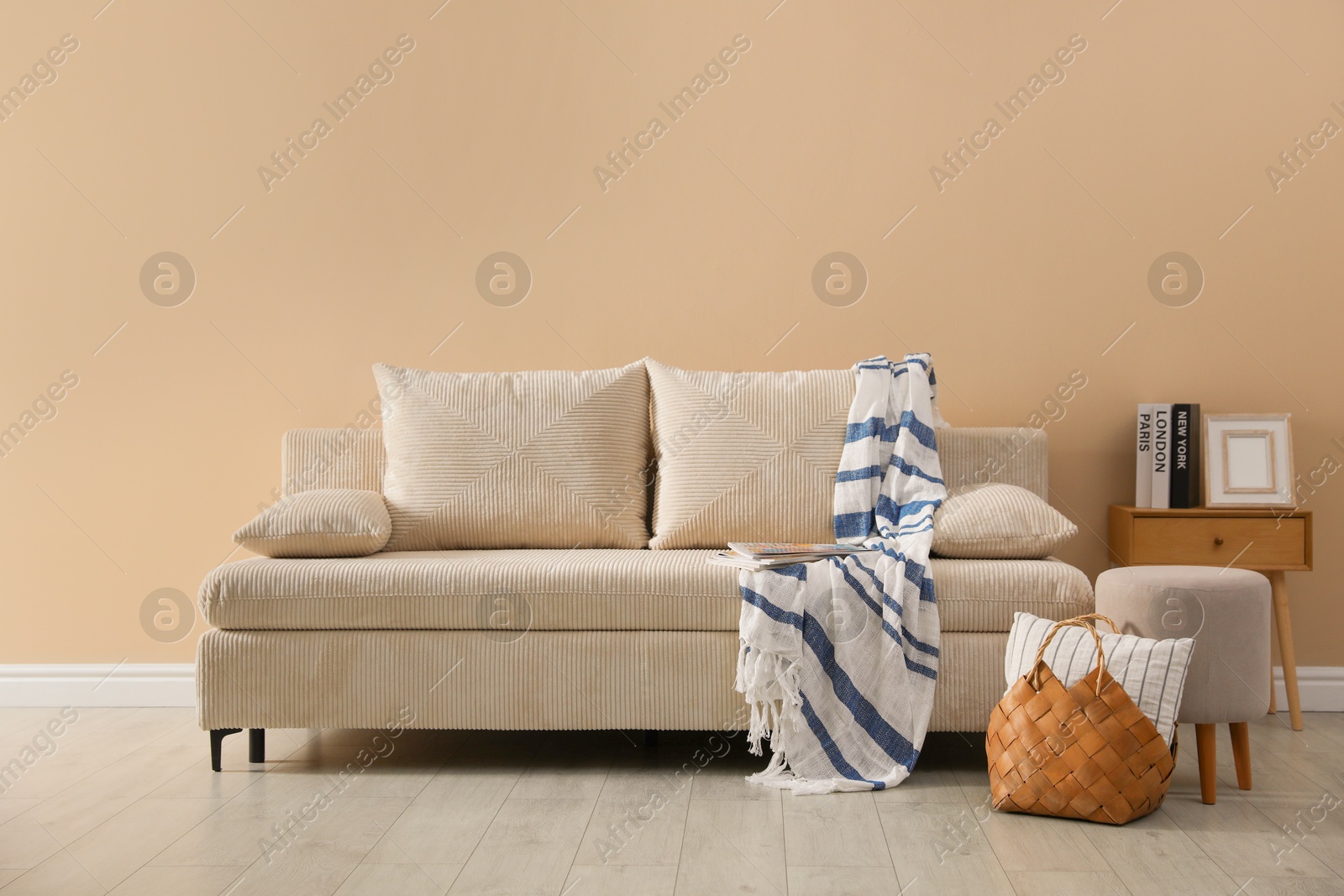 Photo of Comfortable sofa with pillows, blanket, pouf and bag indoors