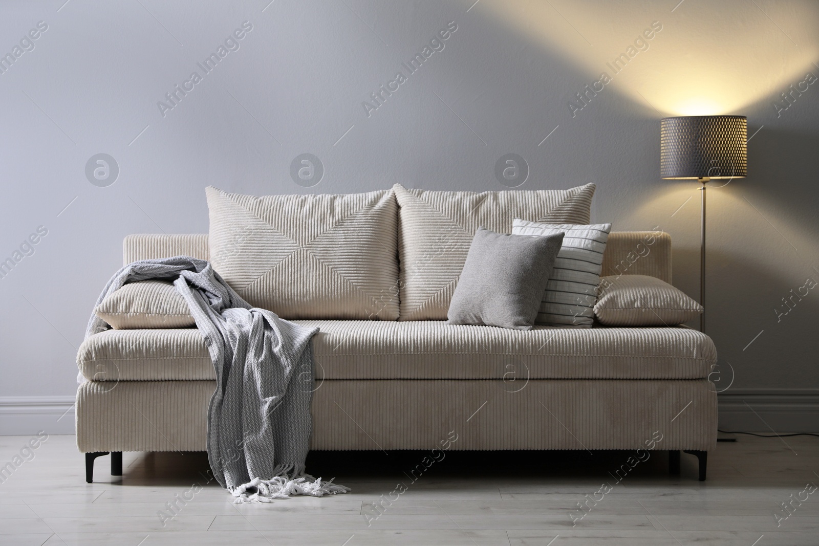 Photo of Comfortable sofa with pillows, blanket and lamp near grey wall indoors