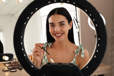 Photo of Beautiful young woman with mascara for eyelashes indoors, view through ring lamp