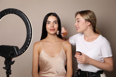 Photo of Professional makeup artist working with beautiful young woman against beige background. Using ring lamp