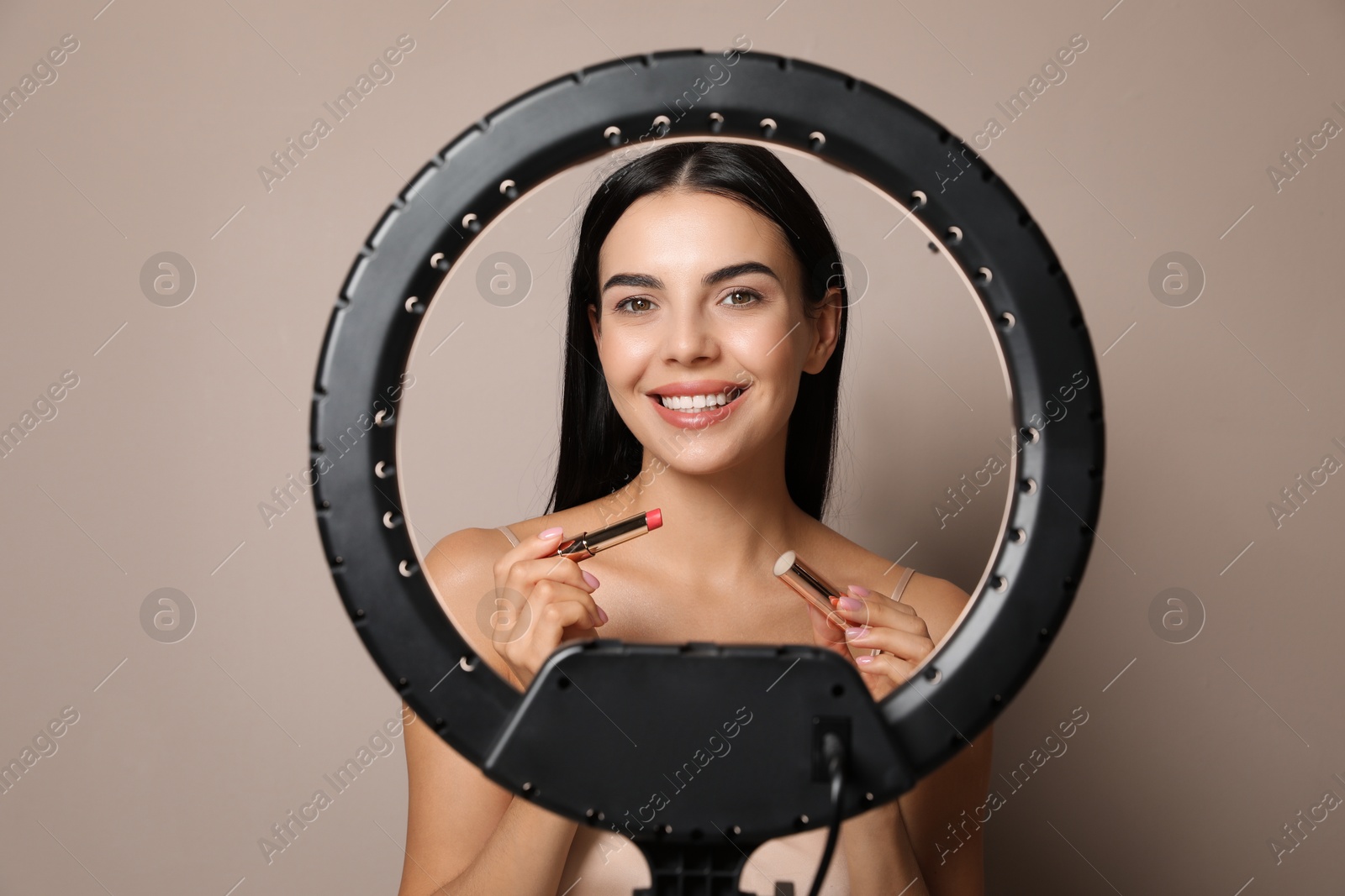 Photo of Beautiful young woman with lipstick on beige background, view through ring lamp