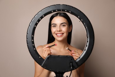 Photo of Beautiful young woman with lipstick on beige background, view through ring lamp