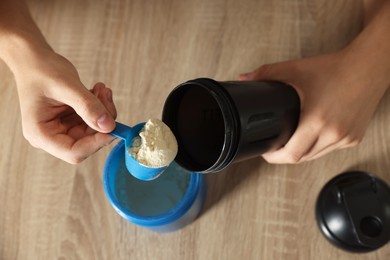 Making protein cocktail. Man adding powder into shaker at wooden table, above view