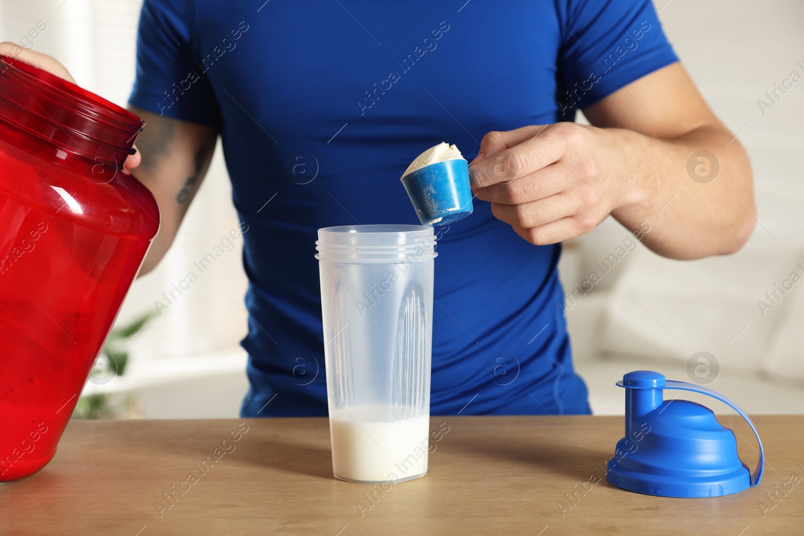 Photo of Making protein cocktail. Man adding powder into shaker at wooden table, closeup