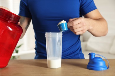 Making protein cocktail. Man adding powder into shaker at wooden table, closeup