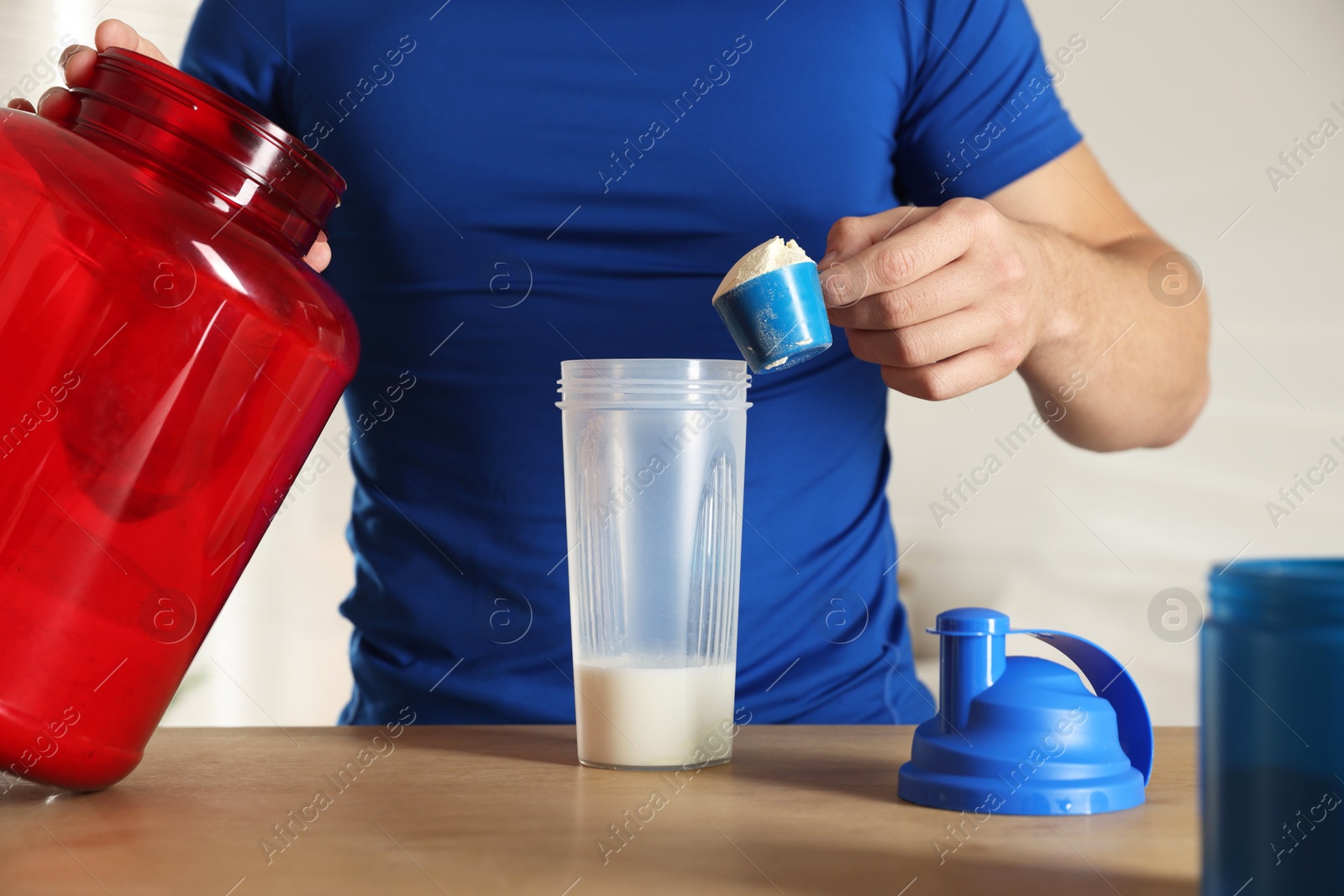 Photo of Making protein cocktail. Man adding powder into shaker at wooden table, closeup