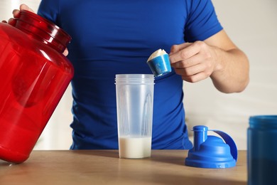 Making protein cocktail. Man adding powder into shaker at wooden table, closeup