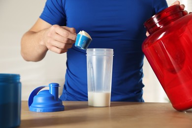 Photo of Making protein cocktail. Man adding powder into shaker at wooden table, closeup