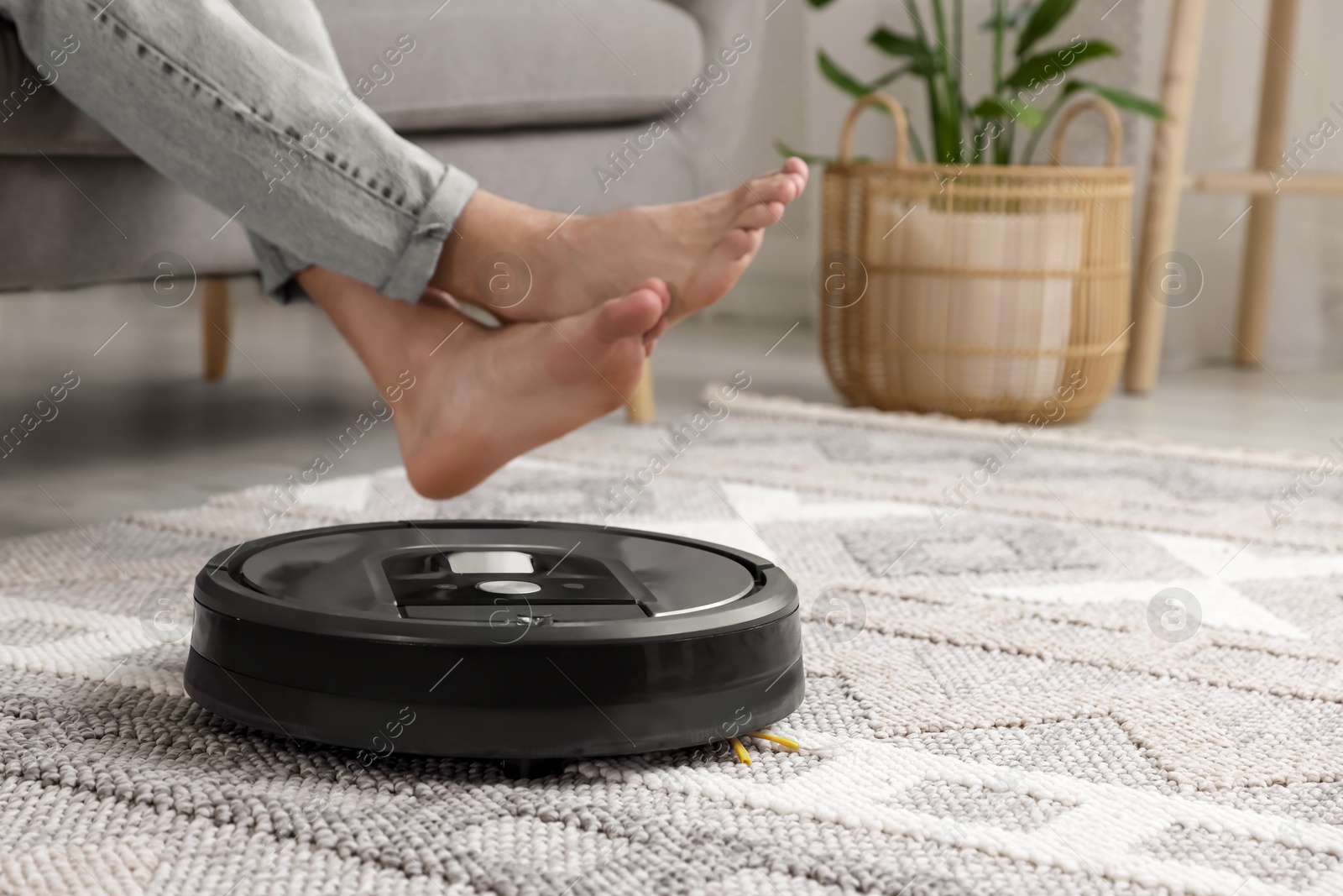 Photo of Young man resting on sofa while robotic vacuum cleaner vacuuming floor at home, closeup