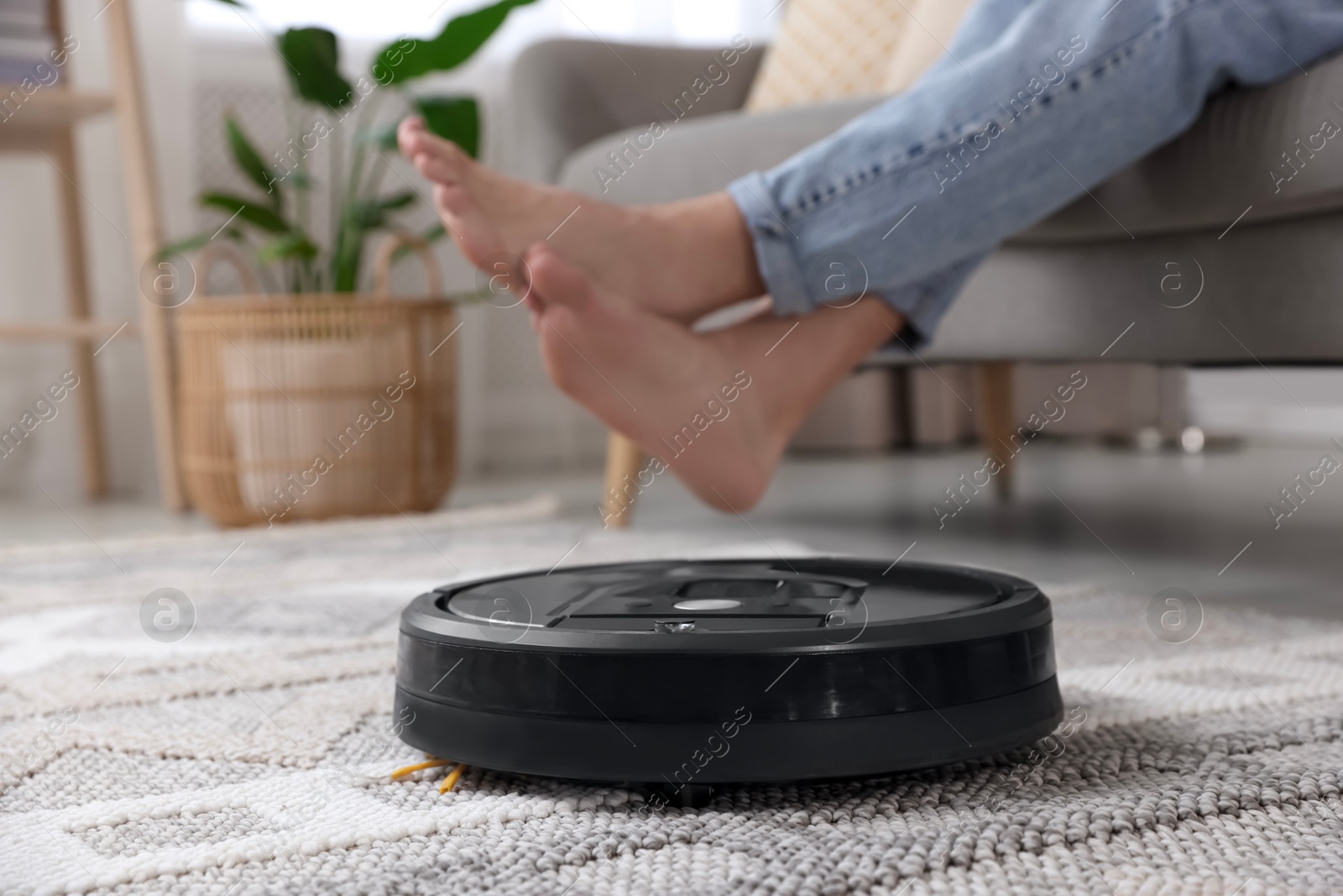 Photo of Young man resting on sofa while robotic vacuum cleaner vacuuming floor at home, closeup