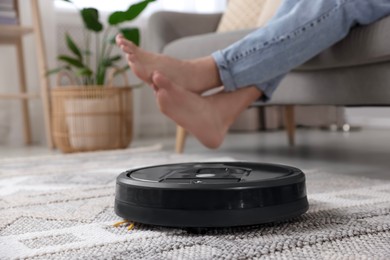 Photo of Young man resting on sofa while robotic vacuum cleaner vacuuming floor at home, closeup