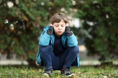 Photo of Autism concept. Lonely little boy covering his ears outdoors