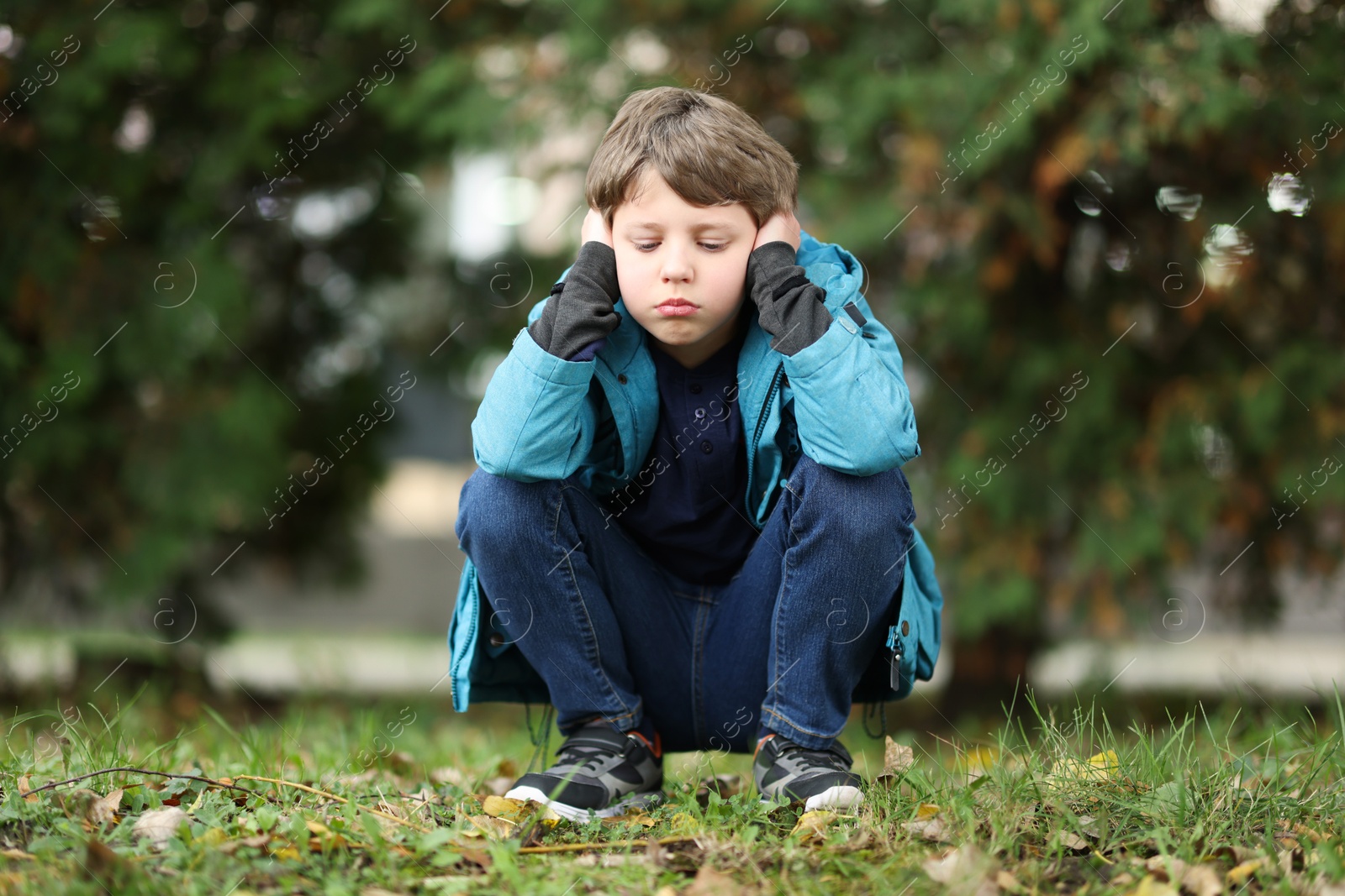 Photo of Autism concept. Lonely little boy covering his ears outdoors