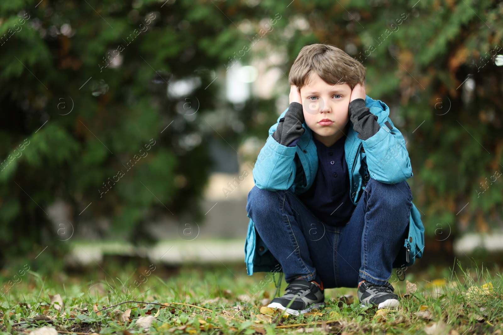 Photo of Autism concept. Lonely little boy covering his ears outdoors, space for text