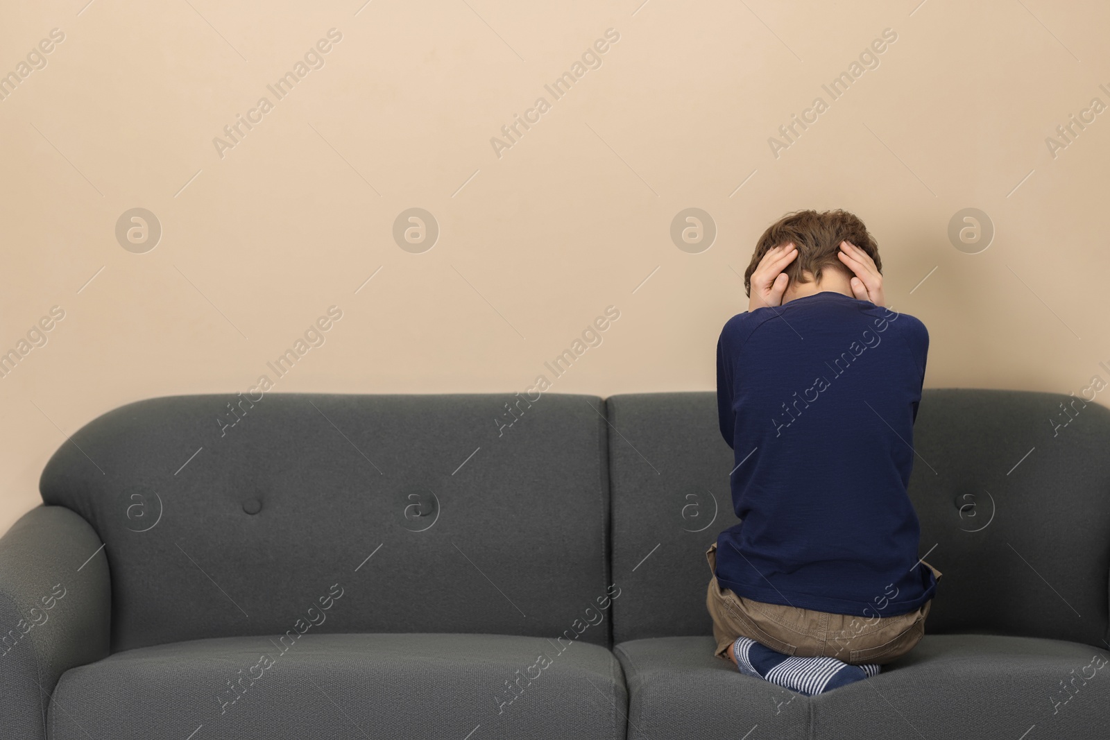 Photo of Autism concept. Lonely little boy covering his ears on sofa at home, back view