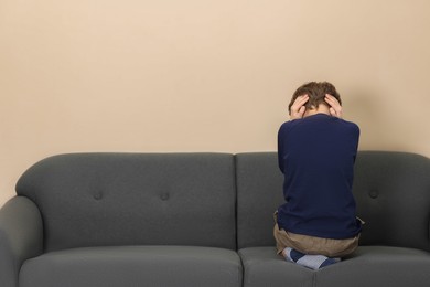 Photo of Autism concept. Lonely little boy covering his ears on sofa at home, back view