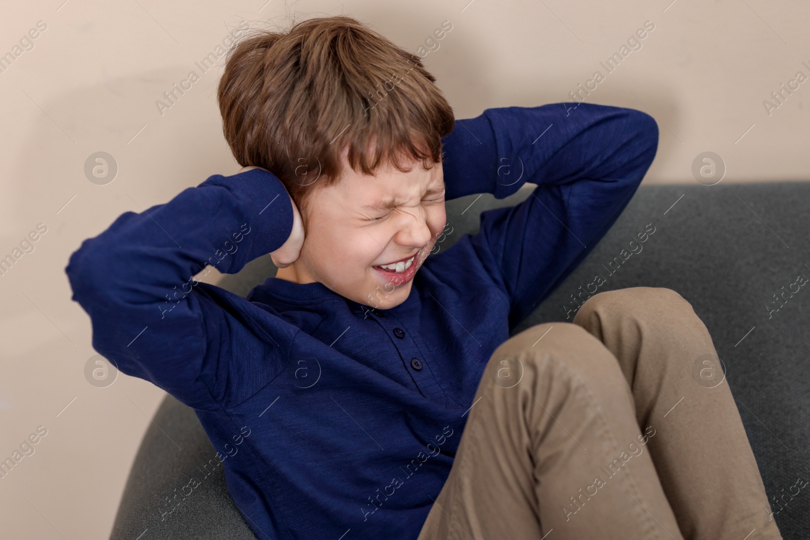 Photo of Autism concept. Scared little boy covering his ears on sofa at home