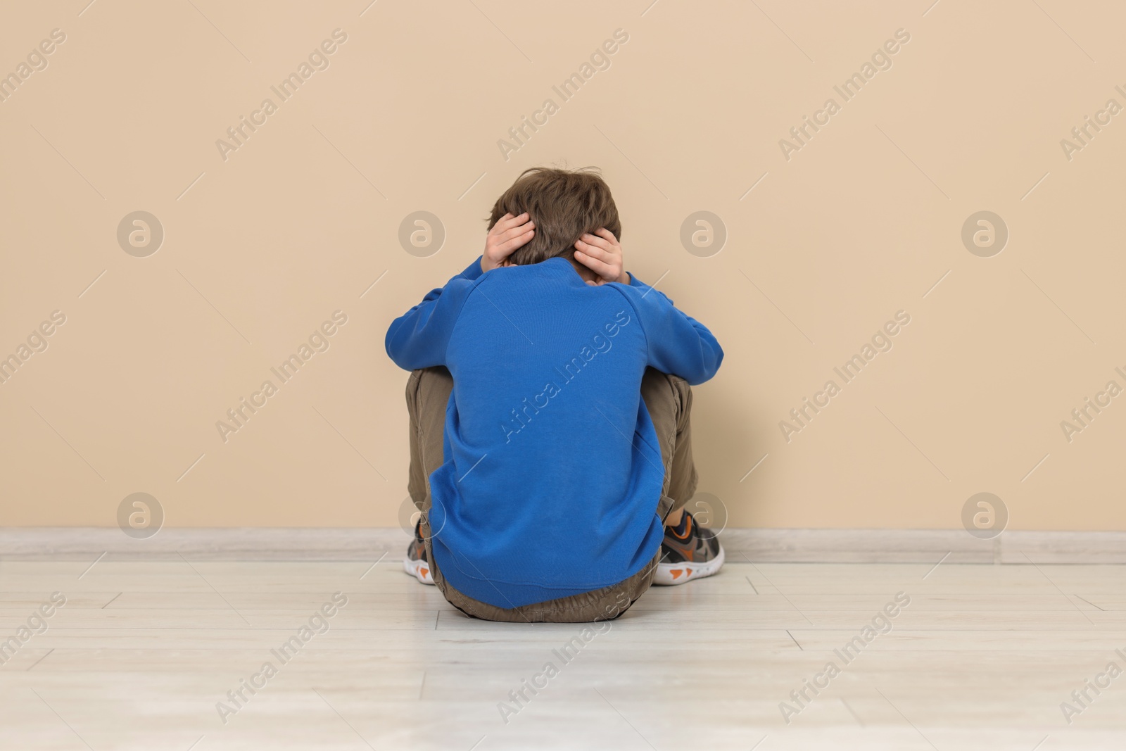 Photo of Autism concept. Lonely little boy covering his ears on floor at home, back view