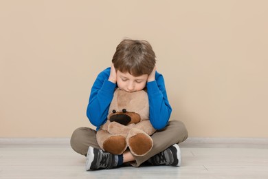 Photo of Autism concept. Lonely little boy with teddy bear covering his ears on floor at home