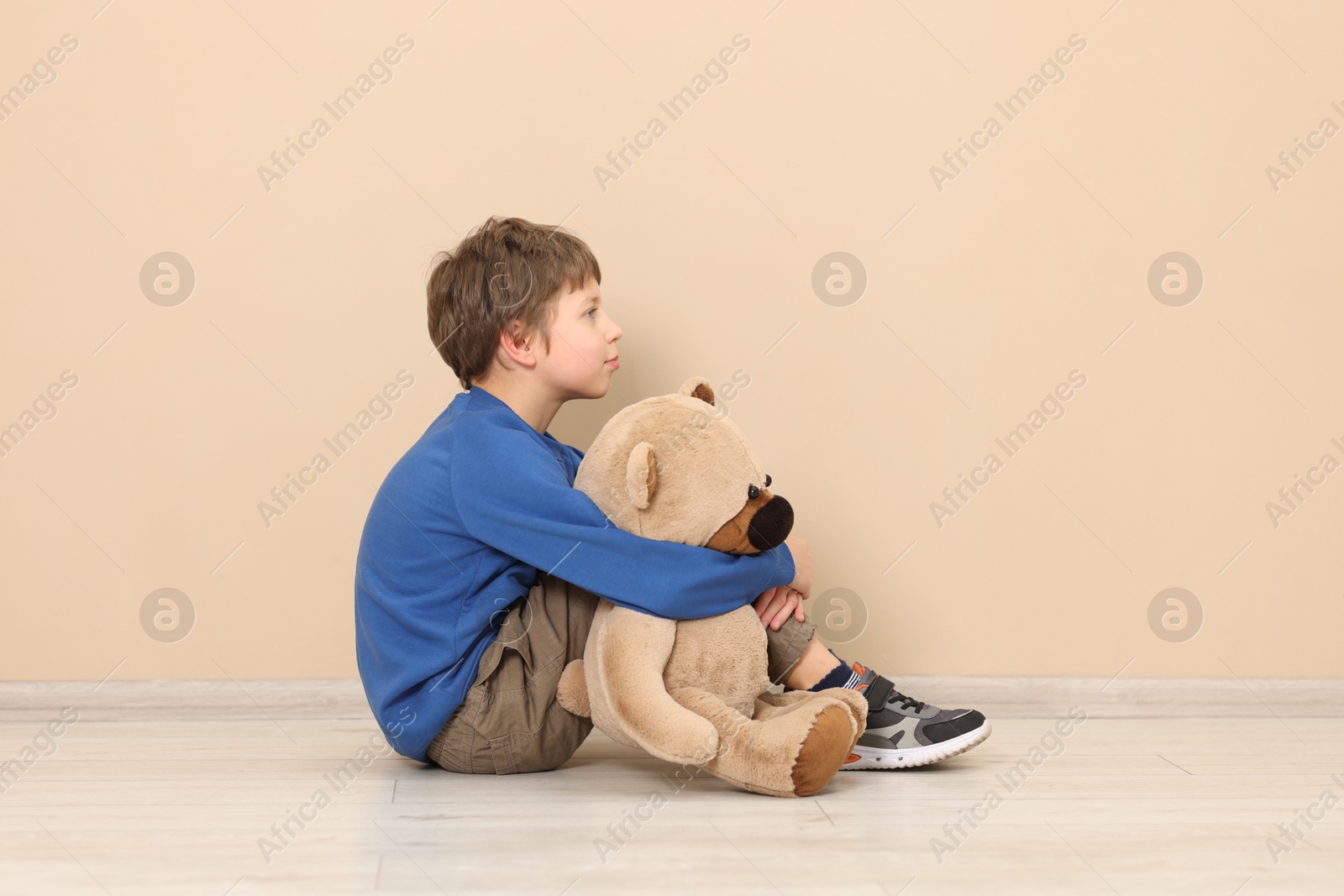 Photo of Autism concept. Lonely little boy with teddy bear on floor at home