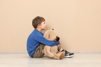 Photo of Autism concept. Lonely little boy with teddy bear on floor at home