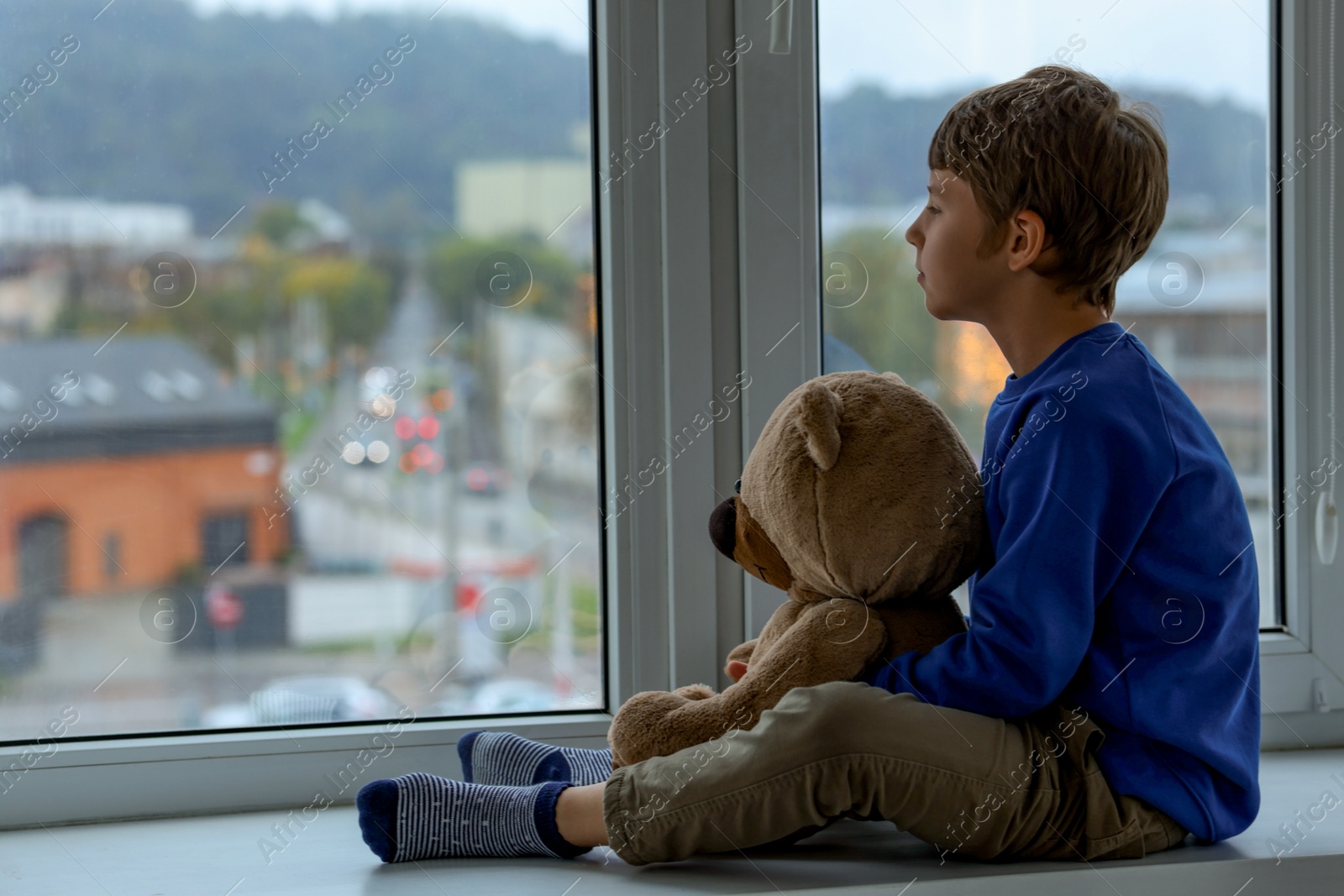 Photo of Autism concept. Lonely little boy with teddy bear near window at home