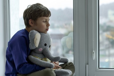 Photo of Autism concept. Lonely little boy with toy elephant near window at home