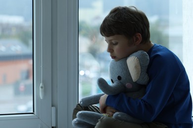 Photo of Autism concept. Lonely little boy with toy elephant near window at home