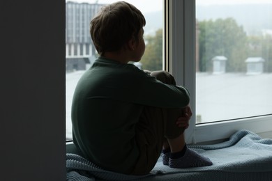 Photo of Autism concept. Lonely little boy near window at home