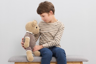 Photo of Autism concept. Lonely little boy with teddy bear on bench at home