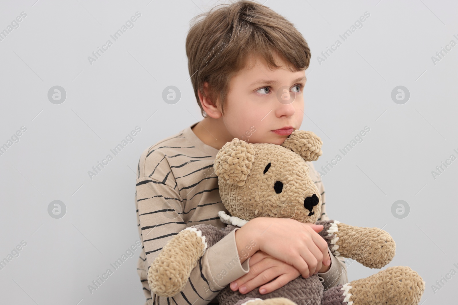 Photo of Autism concept. Lonely little boy with teddy bear on grey background