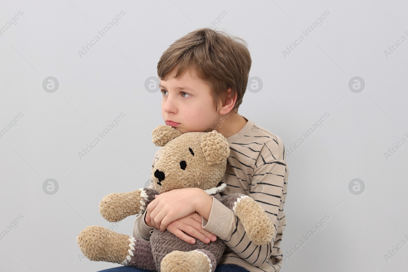 Photo of Autism concept. Lonely little boy with teddy bear on grey background