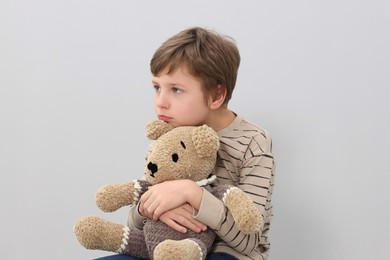 Autism concept. Lonely little boy with teddy bear on grey background