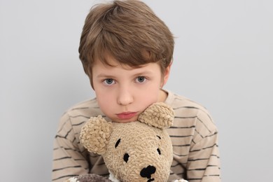 Photo of Autism concept. Lonely little boy with teddy bear on grey background