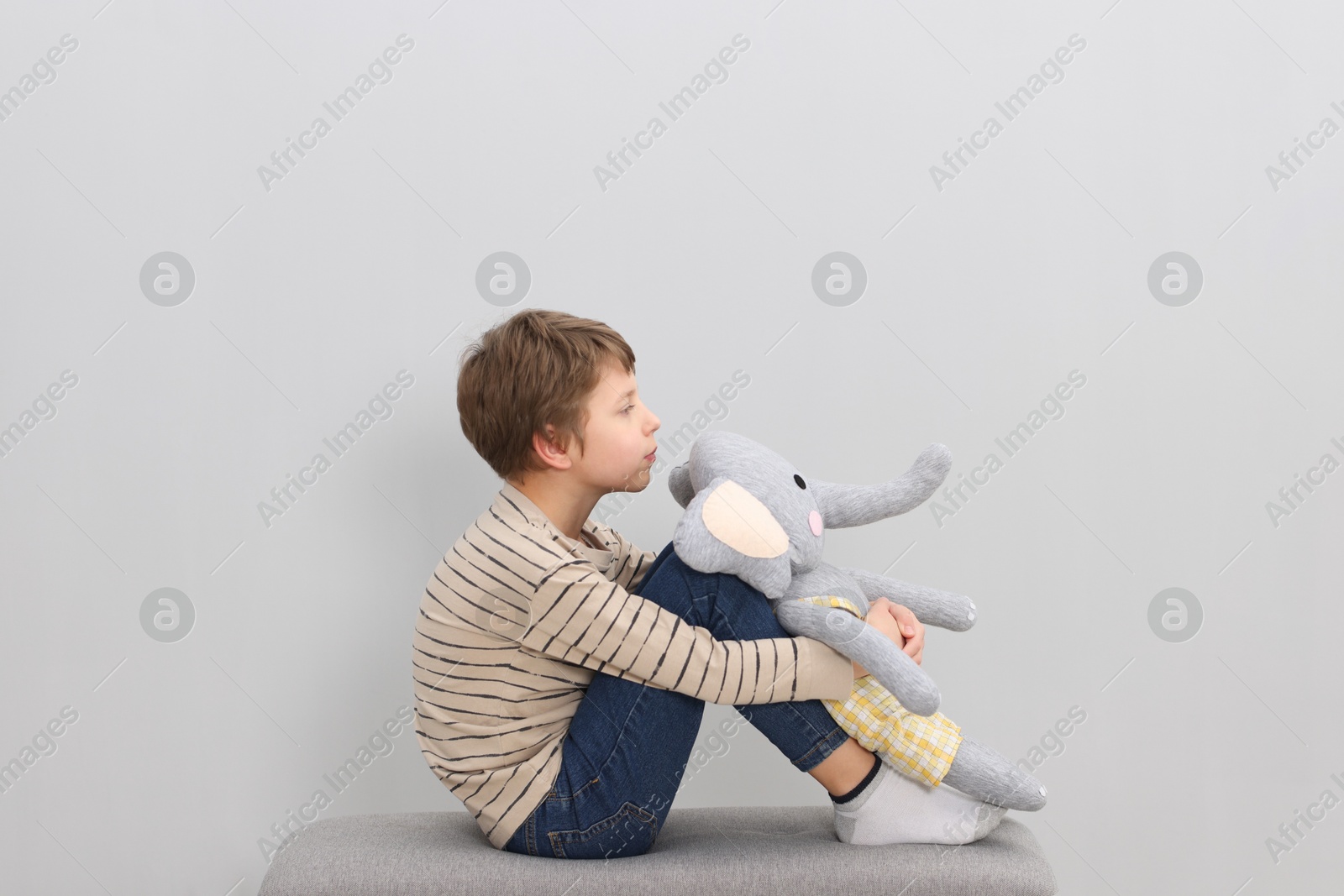 Photo of Autism concept. Lonely little boy with toy elephant on bench at home