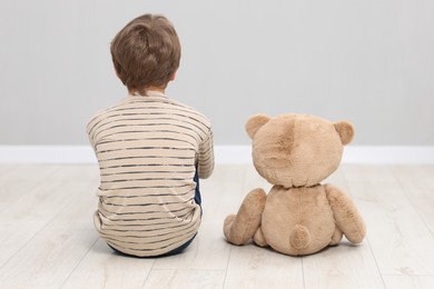 Photo of Autism concept. Lonely little boy with teddy bear on floor at home, back view