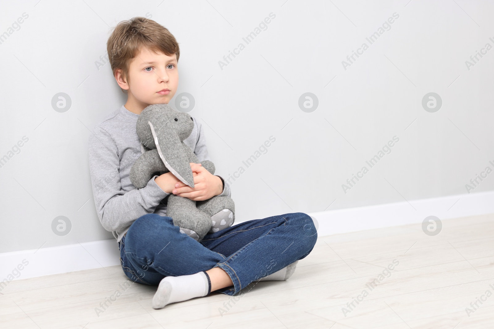 Photo of Autism concept. Lonely little boy with toy bunny on floor near grey wall at home, space for text