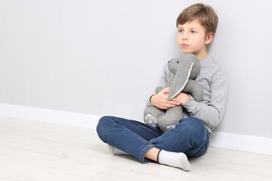 Photo of Autism concept. Lonely little boy with toy bunny on floor near grey wall at home, space for text