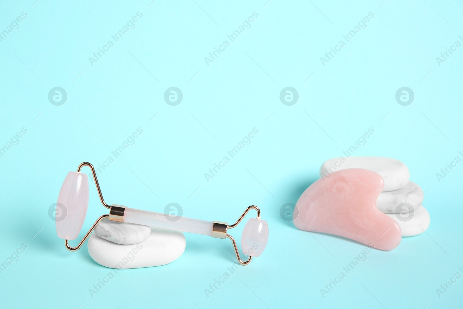 Photo of Rose quartz face roller, gua sha tool and spa stones on light blue background. Space for text