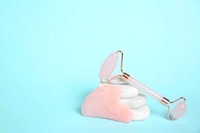 Photo of Rose quartz face roller, gua sha tool and spa stones on light blue background. Space for text