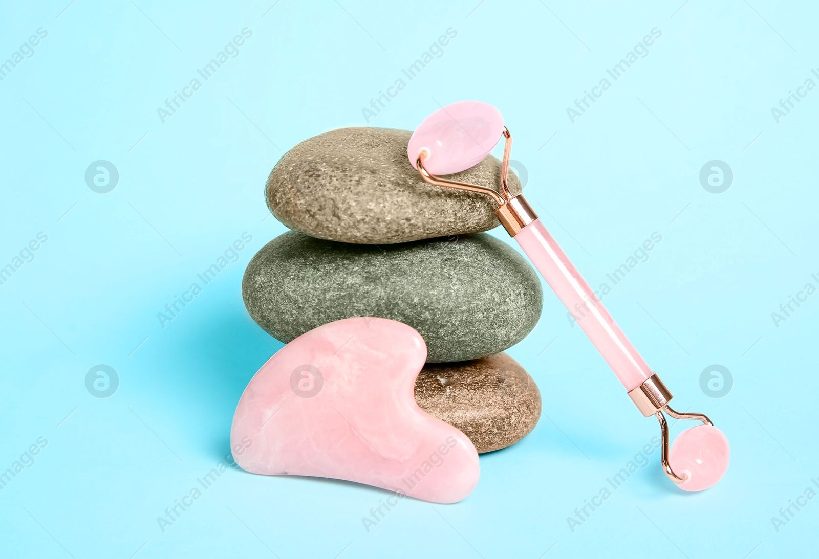 Photo of Rose quartz face roller, gua sha tool and stones on light blue background