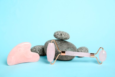 Photo of Rose quartz face roller, gua sha tool and stones on light blue background