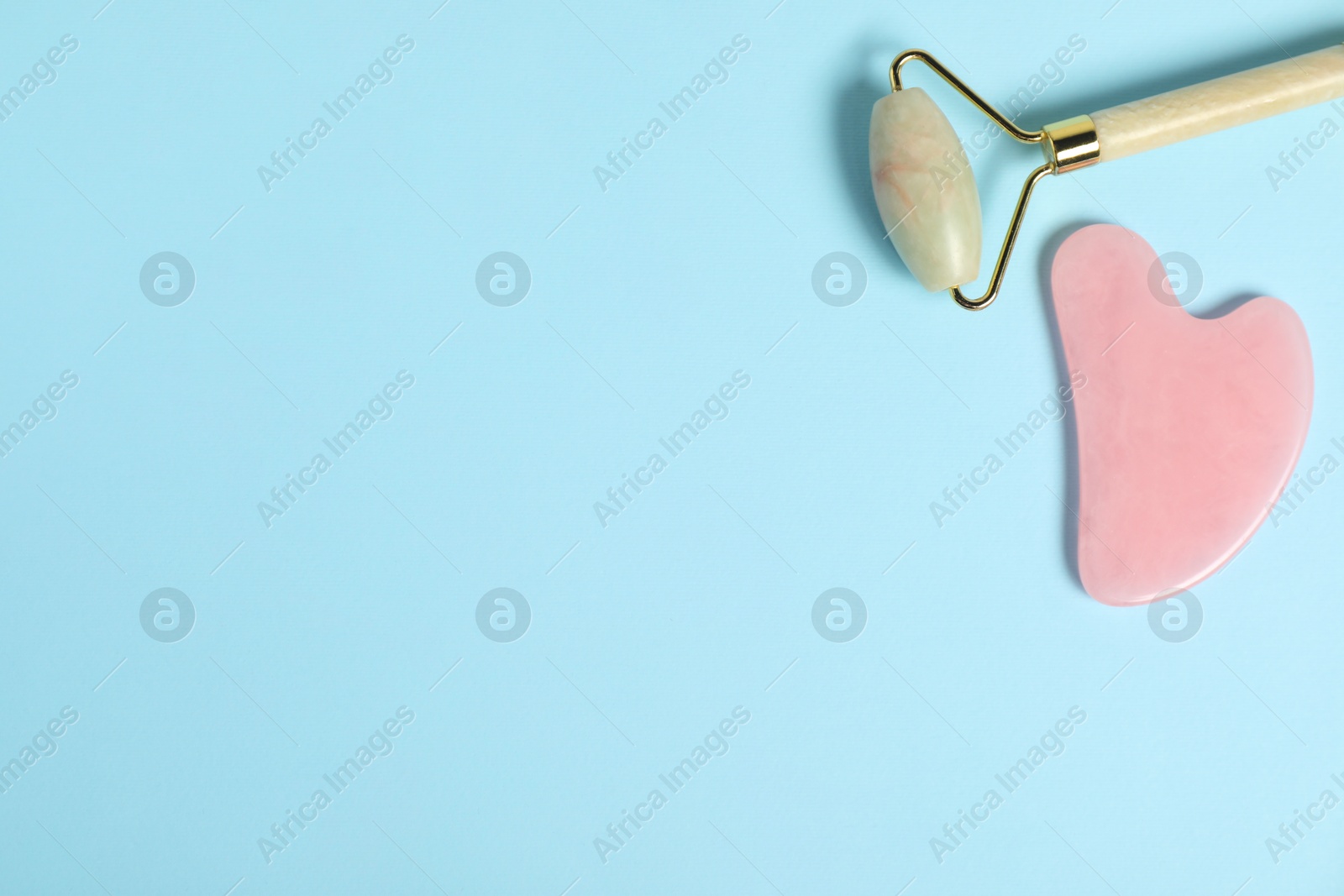 Photo of Face roller and gua sha tool on light blue background, top view. Space for text