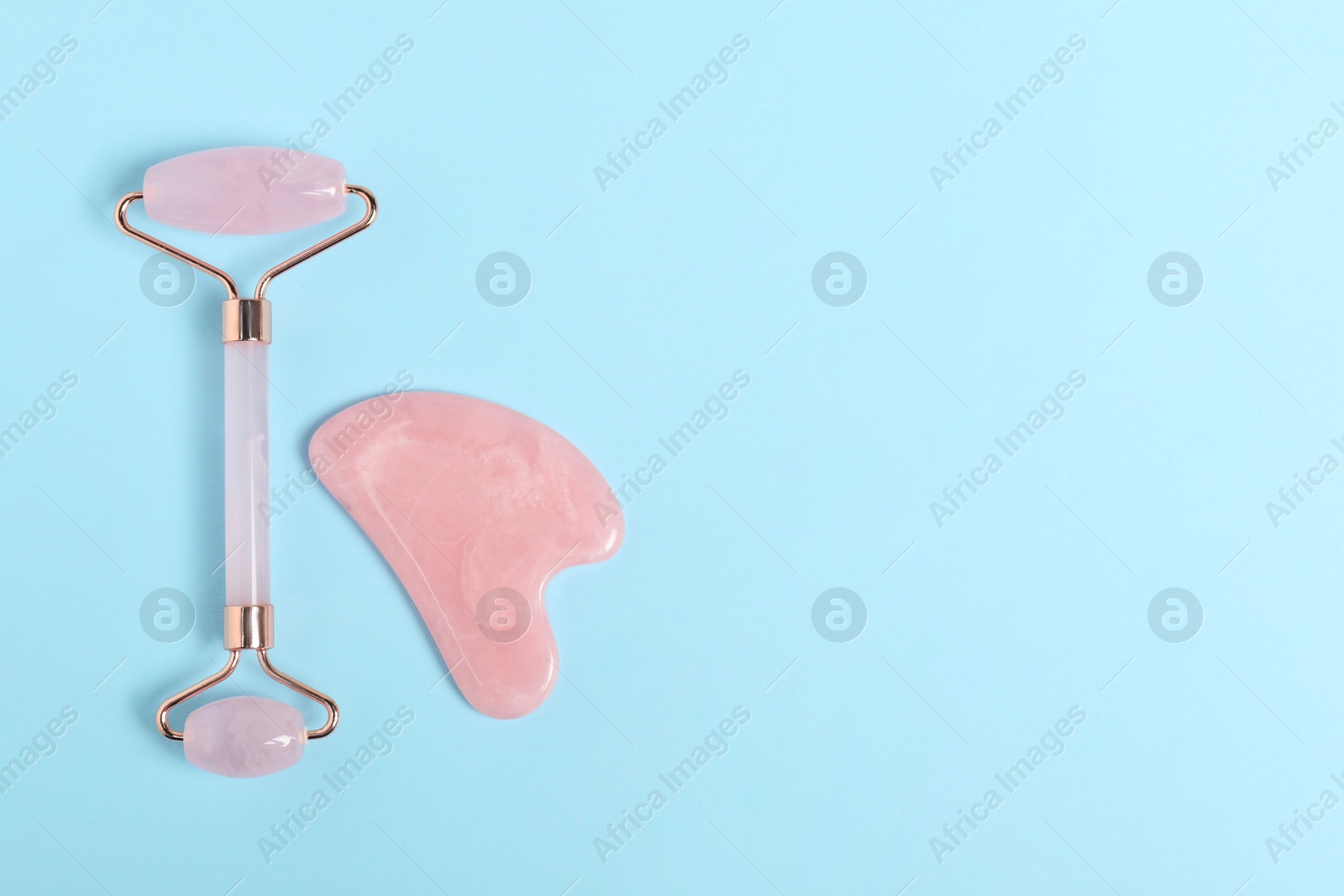 Photo of Face roller and gua sha tool on light blue background, top view. Space for text