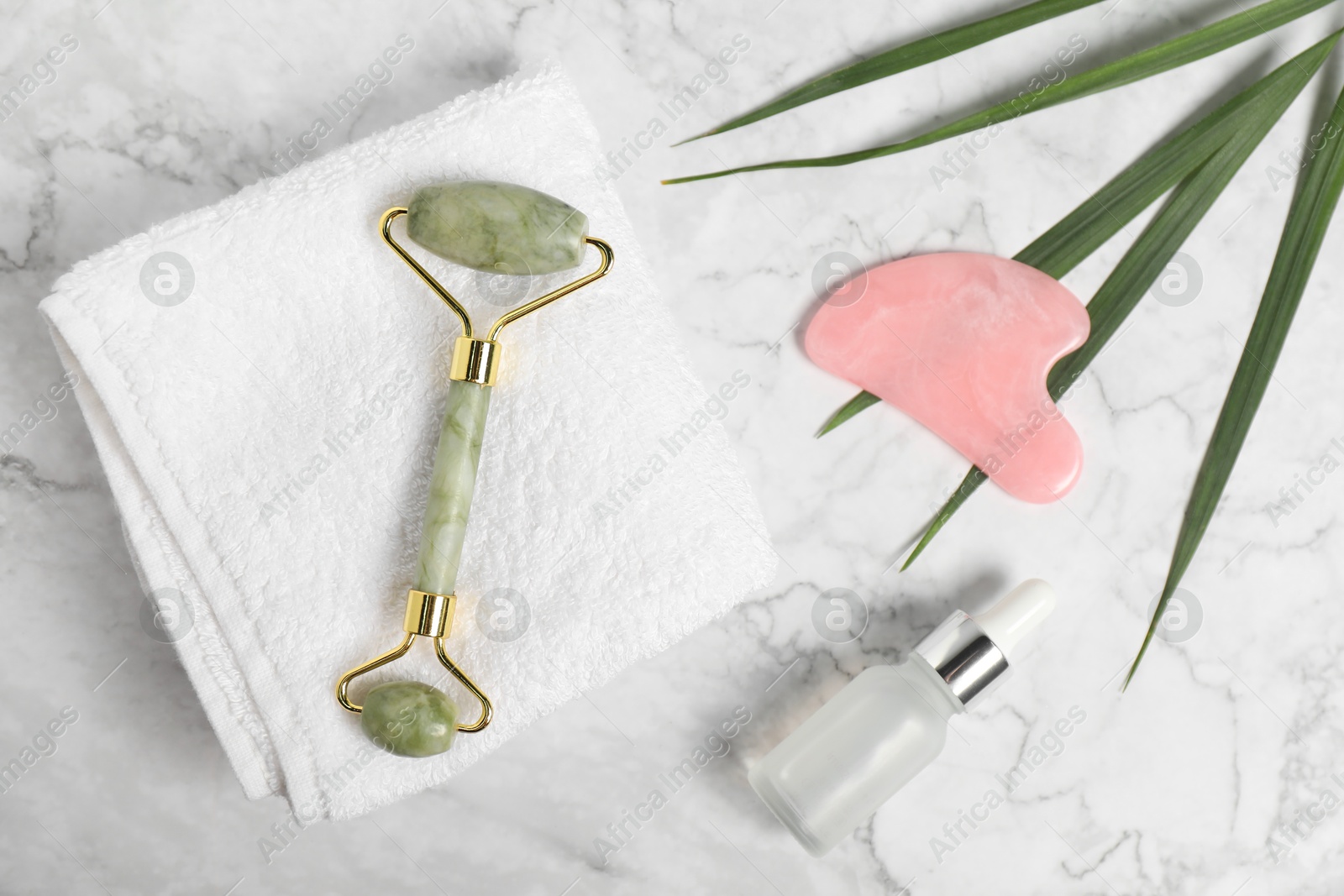 Photo of Face roller, gua sha tool, cosmetic product and towel on white marble background, flat lay