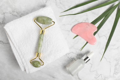 Photo of Face roller, gua sha tool, cosmetic product and towel on white marble background, flat lay